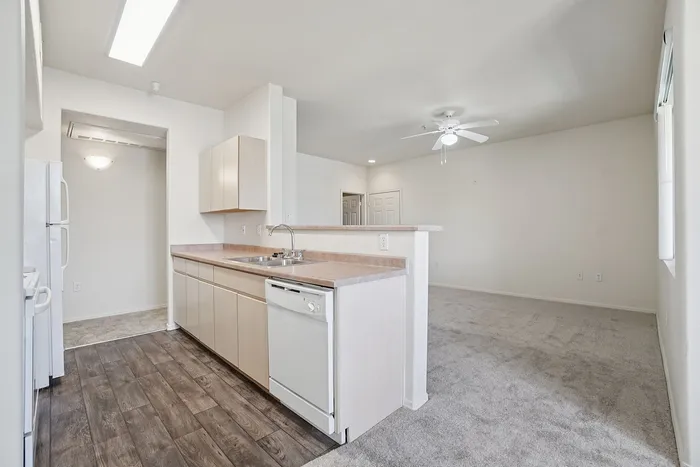 Inviting open-plan kitchen with modern appliances and cozy living area, featuring elegant wood flooring and fresh carpeting.