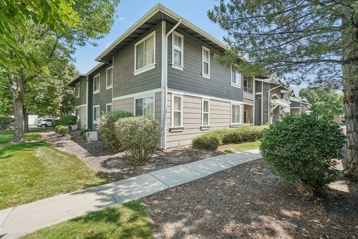 Charming two-story apartment building surrounded by lush greenery and well-maintained pathways, offering a peaceful and inviting atmosphere.