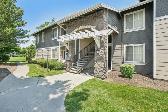 Charming apartment exterior with a stone facade, inviting landscaping, and a welcoming entrance on a sunny day.