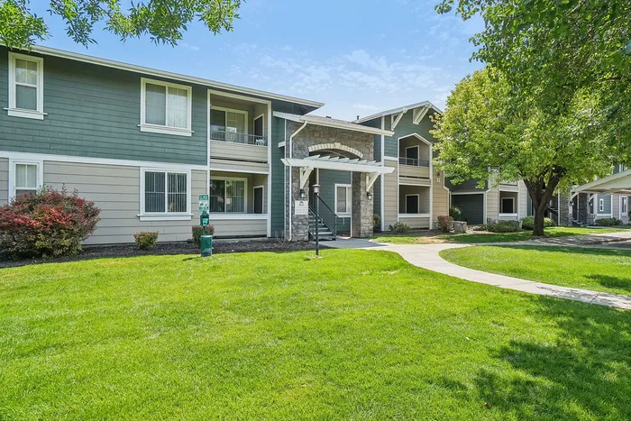 Charming apartment complex with lush green lawns, mature trees, and inviting balcony spaces.