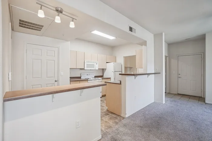 Modern apartment interior showcasing an open kitchen with sleek cabinetry, cozy living area with carpet flooring, and ambient lighting.