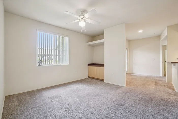 Bright and airy living space with plush carpet, ceiling fan, and ample natural light through large window.