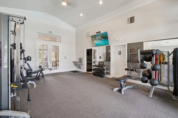 Bright, spacious gym with modern fitness equipment, weight racks, and large mirrors, perfect for a refreshing workout experience.