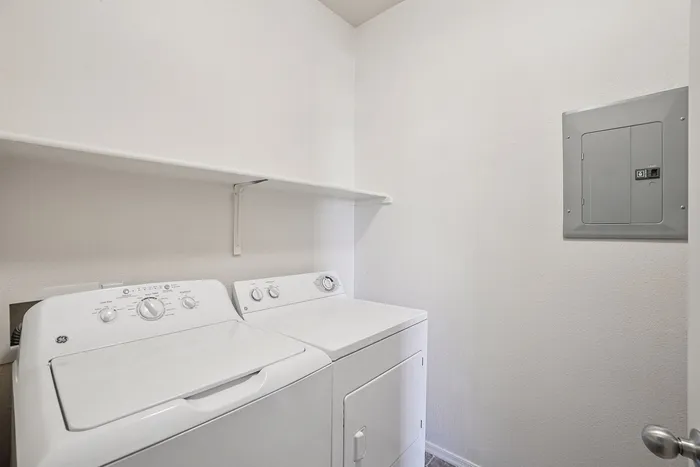 Bright, efficient laundry room featuring modern washer and dryer with convenient wall shelving.
