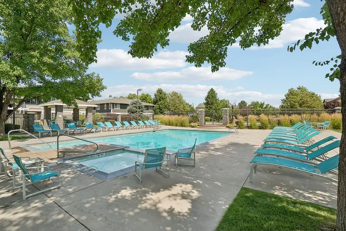 Inviting communal pool surrounded by lush greenery and stylish lounge chairs, offering a perfect retreat under a blue sky.