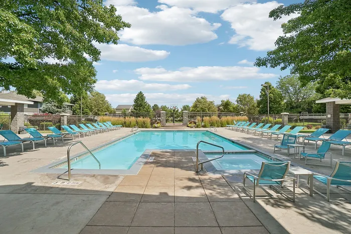 Inviting outdoor pool area with bright blue lounge chairs, surrounded by lush greenery and a clear blue sky.