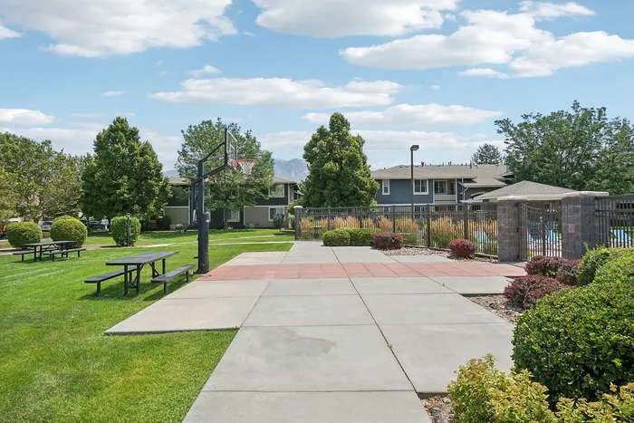 Charming outdoor space with a basketball court, picnic tables, and lush landscaping in a serene apartment community.