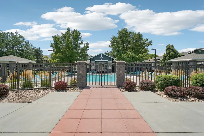 Inviting community pool area surrounded by manicured landscaping and cozy lounging spaces under a clear blue sky.