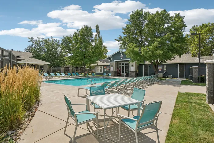 Inviting outdoor pool area with ample seating, surrounded by lush greenery and modern clubhouse, ideal for relaxation and social gatherings.