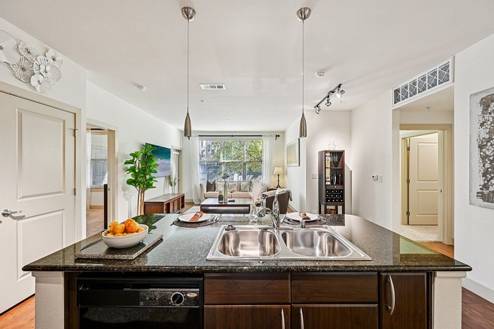 Bright open-plan apartment with a modern kitchen island overlooking a cozy living area, featuring stylish pendant lighting and elegant decor.