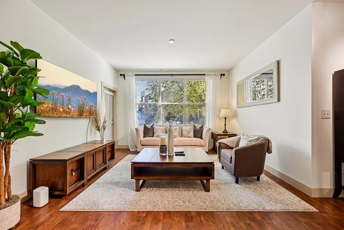 Inviting living room with elegant decor, featuring cozy seating arrangements, a large window with natural light, and sleek wooden furniture.