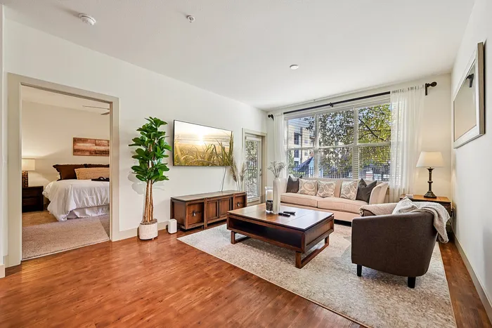 Inviting apartment living room featuring a cozy seating area, elegant wooden floors, and abundant natural light pouring through large windows.