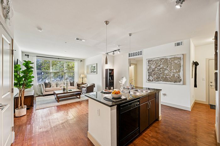 Inviting open-concept apartment showcasing a modern kitchen with granite countertops and a cozy living room with large windows and stylish decor.