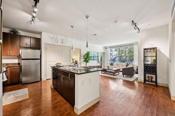 Modern apartment interior featuring a sleek kitchen with stainless steel appliances, an island with pendant lighting, and an inviting living room with large windows and elegant decor.