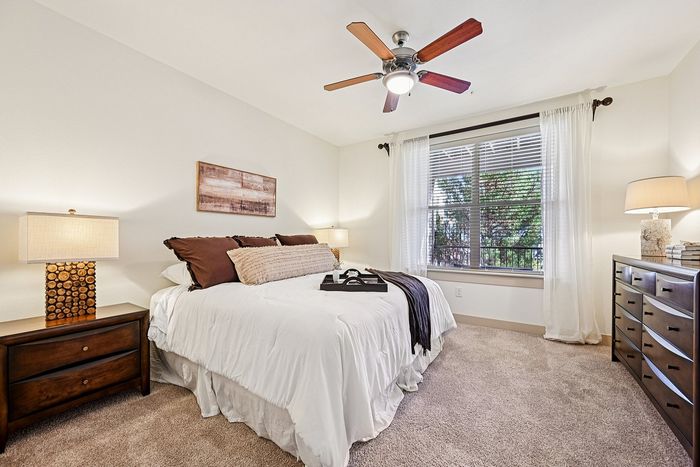 Bright and inviting bedroom with a large window, elegant decor, and plush carpet, offering a serene retreat.