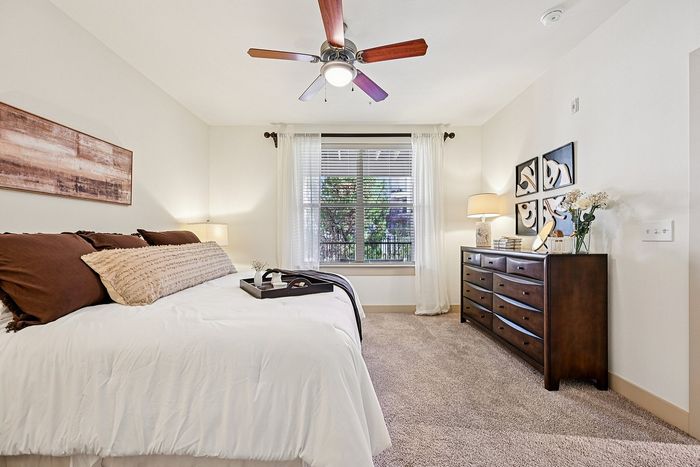 Inviting bedroom with a cozy ambience, featuring a plush bed, elegant wooden dresser, and soothing natural light through large windows.