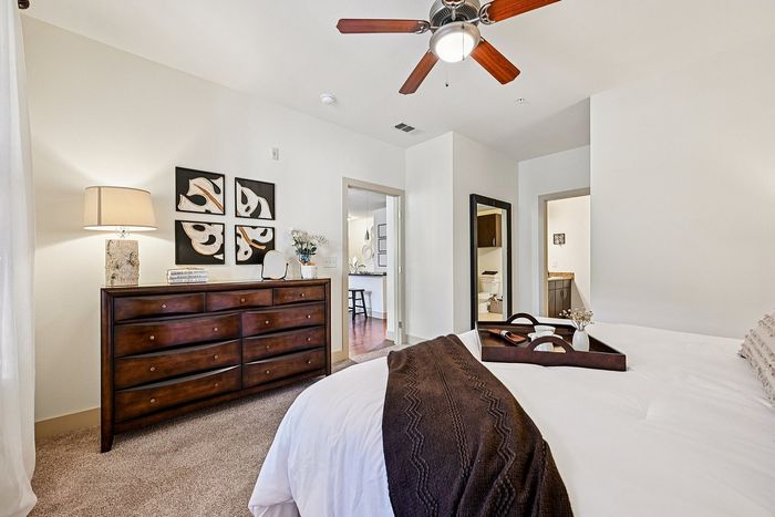 Elegant bedroom showcasing a cozy bed with plush bedding, wooden dresser, stylish wall art, and an attached bathroom, exuding warmth and comfort.