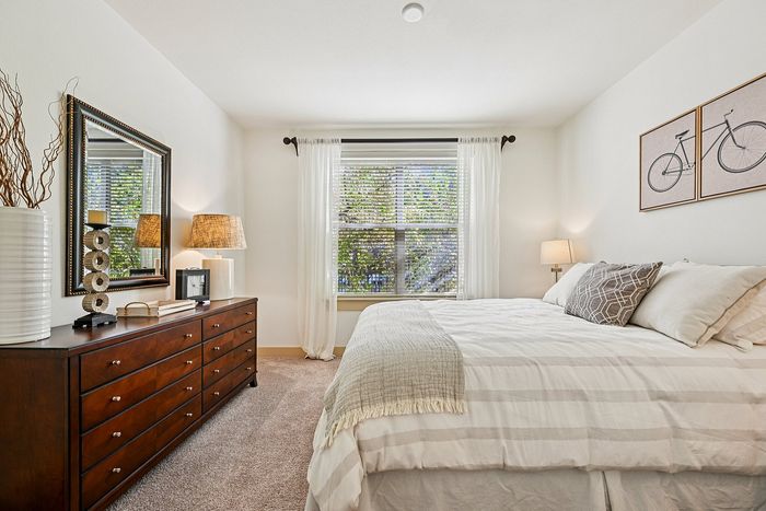 Bright and inviting bedroom with elegant decor, featuring a cozy bed, stylish dresser, and large window with scenic views.