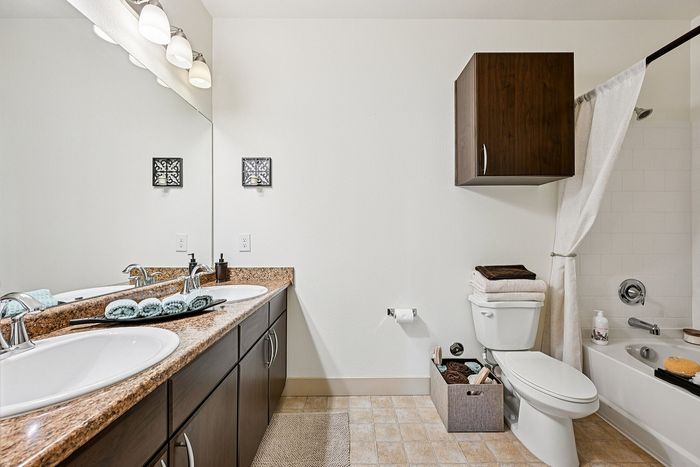 Bright and modern bathroom featuring elegant double sinks, sleek cabinetry, and a cozy bathtub with stylish fixtures.