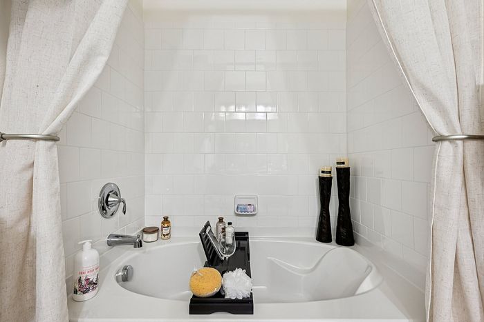 Luxurious white tiled bathroom featuring an elegant bathtub with a sleek tray, surrounded by stylish candles and accents for a serene spa-like experience.