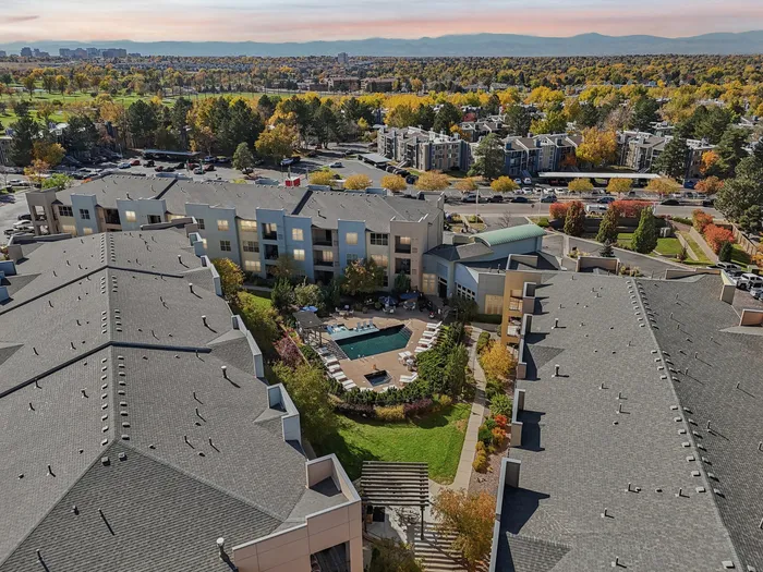 Breathtaking aerial view of a modern apartment complex with a central courtyard and swimming pool, surrounded by lush greenery and scenic mountain backdrop.
