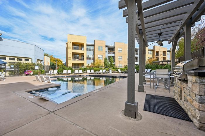 Inviting apartment complex with a luxurious pool, modern lounge chairs, and a stylish outdoor barbecue area, perfect for relaxation and entertainment.