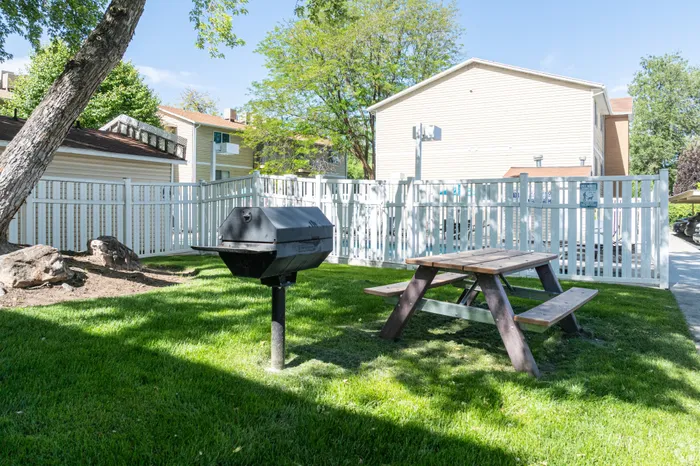 Charming outdoor space with a barbecue grill, picnic table, and lush greenery, perfect for gatherings.