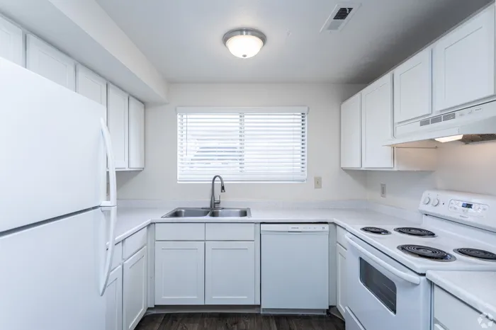 Bright and modern kitchen with sleek white cabinetry, stainless steel sink, and large window for natural light.
