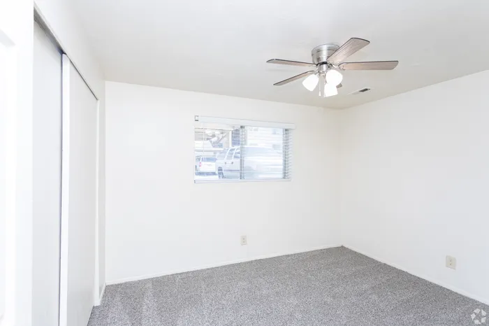 Spacious, bright bedroom with modern ceiling fan, cozy carpet, and ample natural light through a large window.
