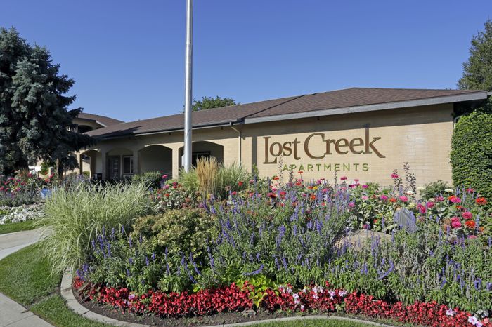 Lost Creek Apartments exterior with vibrant garden and welcoming facade under a clear blue sky.