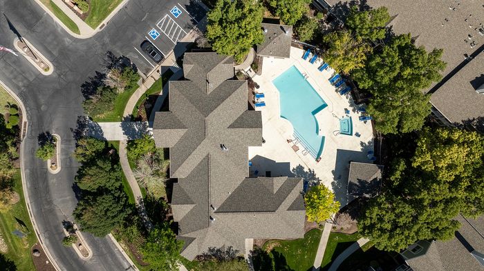 Aerial view of a luxurious apartment complex featuring a sparkling swimming pool, lush greenery, and ample parking spaces.