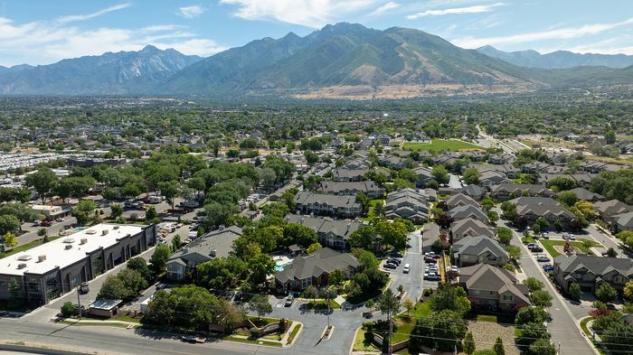 Scenic aerial view of a vibrant suburban neighborhood nestled against picturesque mountains, showcasing lush green spaces and modern homes.