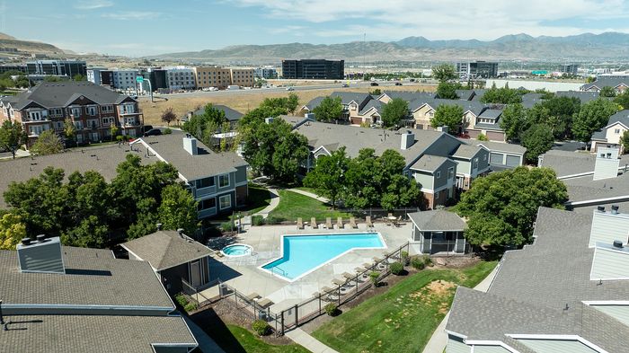 Aerial view of charming residential community with a sparkling swimming pool, lush green landscaping, and scenic mountain backdrop.