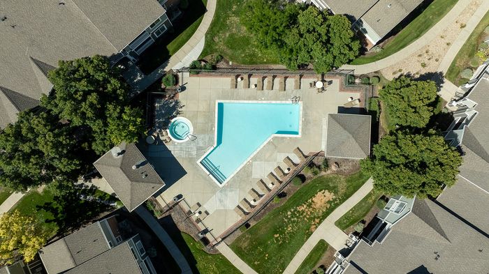 Aerial view of a luxurious apartment complex featuring a spacious outdoor pool and cozy hot tub surrounded by modern landscaping and green spaces.