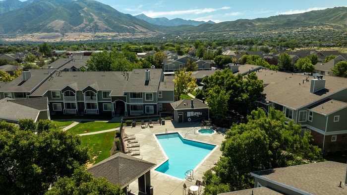 Scenic aerial view of a charming apartment complex with a stunning mountain backdrop, featuring a refreshing pool, lush greenery, and inviting outdoor spaces.