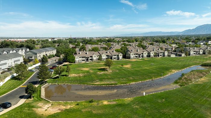 Serene apartment complex surrounded by lush green lawns and a tranquil pond, set against a backdrop of scenic mountain views.