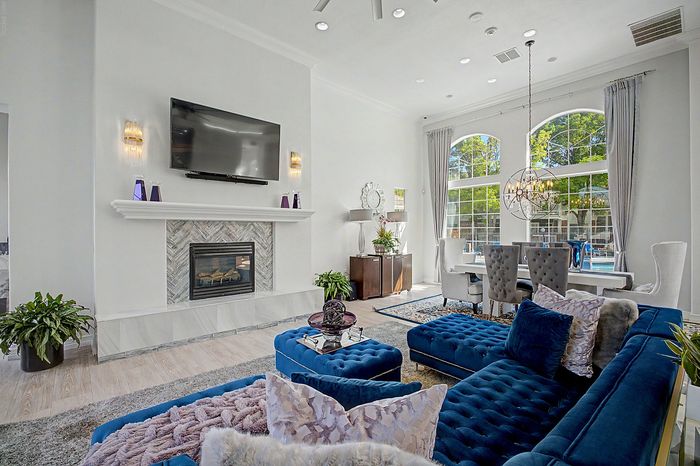 Luxurious living room with elegant blue velvet furniture, a modern fireplace, and large arched windows providing abundant natural light, overlooking a swimming pool.
