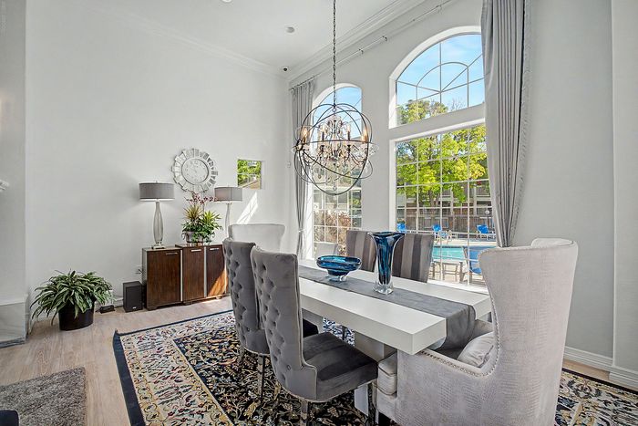 Elegant dining room with plush velvet chairs, a chic chandelier, and large arched windows offering poolside views.