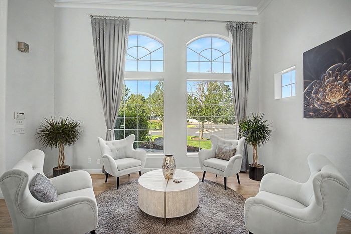Elegantly designed living room with plush white armchairs, chic decor, and large arched windows offering scenic views and abundant natural light.