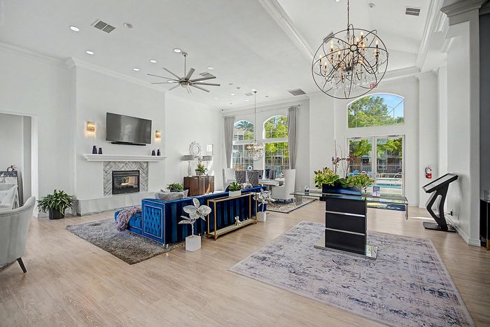 Luxurious living room with high ceilings, elegant chandelier, plush seating, and modern fireplace, offers a stylish ambiance with natural light through large arched windows.