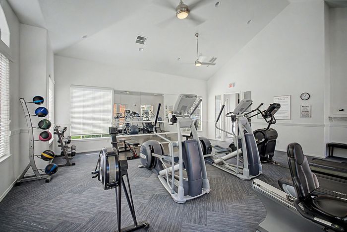Modern apartment fitness center featuring state-of-the-art exercise machines, including treadmills and elliptical trainers in a bright, inviting space with large windows.