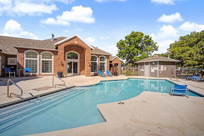 Inviting outdoor pool area with lounge chairs, set against a backdrop of a charming brick clubhouse and sunny skies.