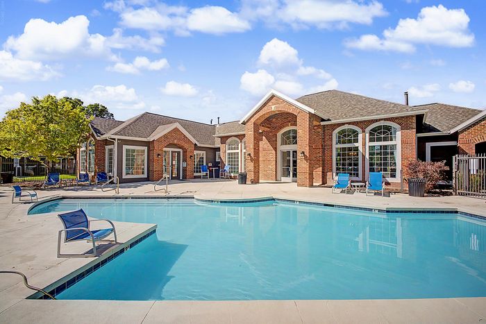 Charming apartment complex featuring a sparkling outdoor pool surrounded by elegant brick architecture and lush greenery.