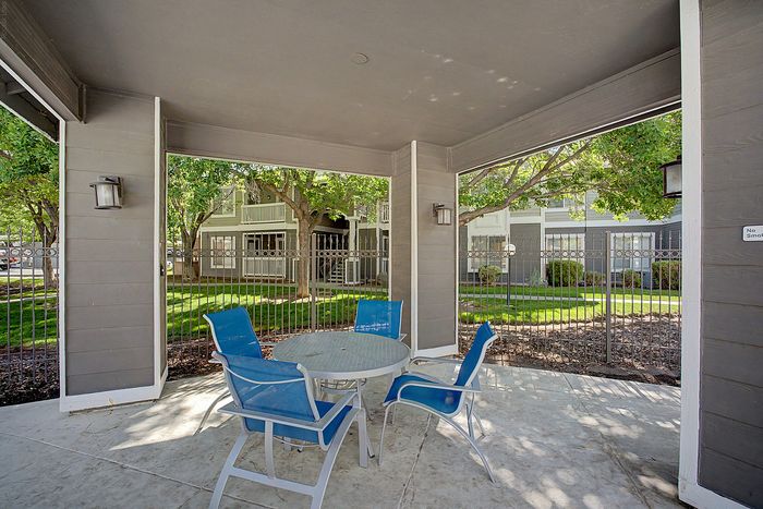 Inviting outdoor patio with modern furniture, set against a backdrop of lush greenery and stylish apartment buildings.