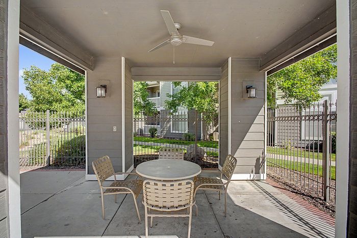 Charming covered patio with a cozy seating area, ceiling fan, and view of lush greenery, perfect for relaxing in style.