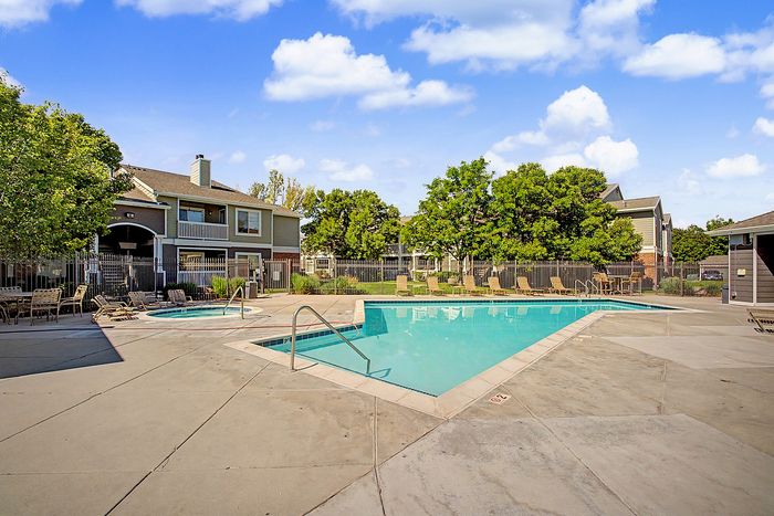 Sunny apartment complex with a sparkling swimming pool and lush green surroundings, perfect for relaxation and leisure.