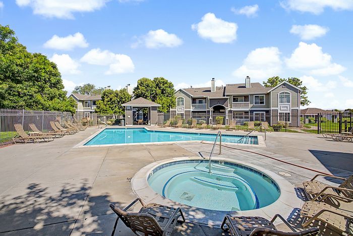 Inviting community swimming pool and hot tub surrounded by lounge chairs, set against a backdrop of charming residential buildings and lush greenery.