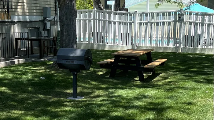 Inviting lush green lawn, elegant white fence, and a cozy picnic table under dappled shade.