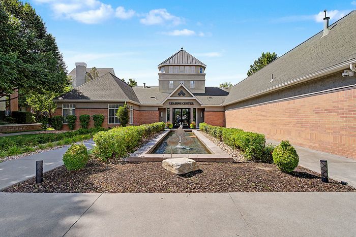 Charming leasing center entrance surrounded by lush greenery and a contemporary water feature, offering a welcoming atmosphere.