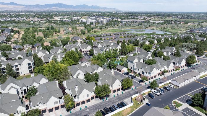 Scenic aerial view of a charming suburban neighborhood with well-maintained apartments, lush greenery, and panoramic mountain views.